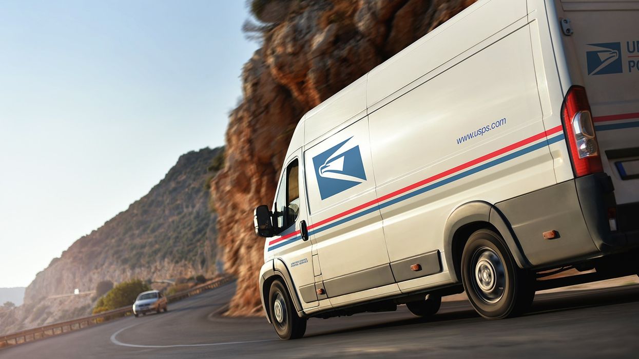A United States Postal Service van drives on a curving mountain road..